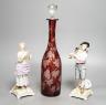 A late 19th century Bohemian wheel engraved ruby glass decanter and a pair of continental porcelain figures, decanter 37 cms high, including stopper.                                                                       