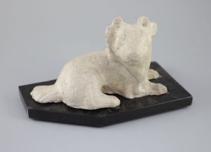 A Chinese grey pottery figure of a recumbent dog, Han dynasty or later 23.5cm long, wood stand                                         