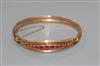 An early 20th century yellow metal and graduated red stone (including doublets) set hinged bangle.                                     