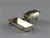 An Edwardian novelty silver pin cushion, modelled as a pig at a trough, by Adie & Lovekin, Birmingham, 1907, trough 56mm.              