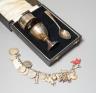 A 1930's cased silver christening set, comprising an egg cup, spoon and napkin ring, together with a white metal charm bracelet hung with assorted charms and coins including silver.                                       