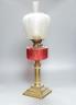 A brass and cranberry glass oil lamp with shade and chimney, total height 66cm                                                                                                                                              
