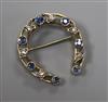 A yellow metal, sapphire and diamond horseshoe brooch, 30mm.                                                                           