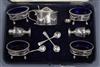 A cased George V Goldsmiths & Silversmiths seven piece Adam style silver condiment set.                                                