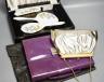 A boxed, three piece silver plated translucent enamelled dressing set, a purple leather stationary case and an evening bag                                                                                                  