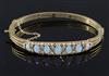 A 20th century pierced gold and graduated seven stone white opal set hinged bracelet,                                                  