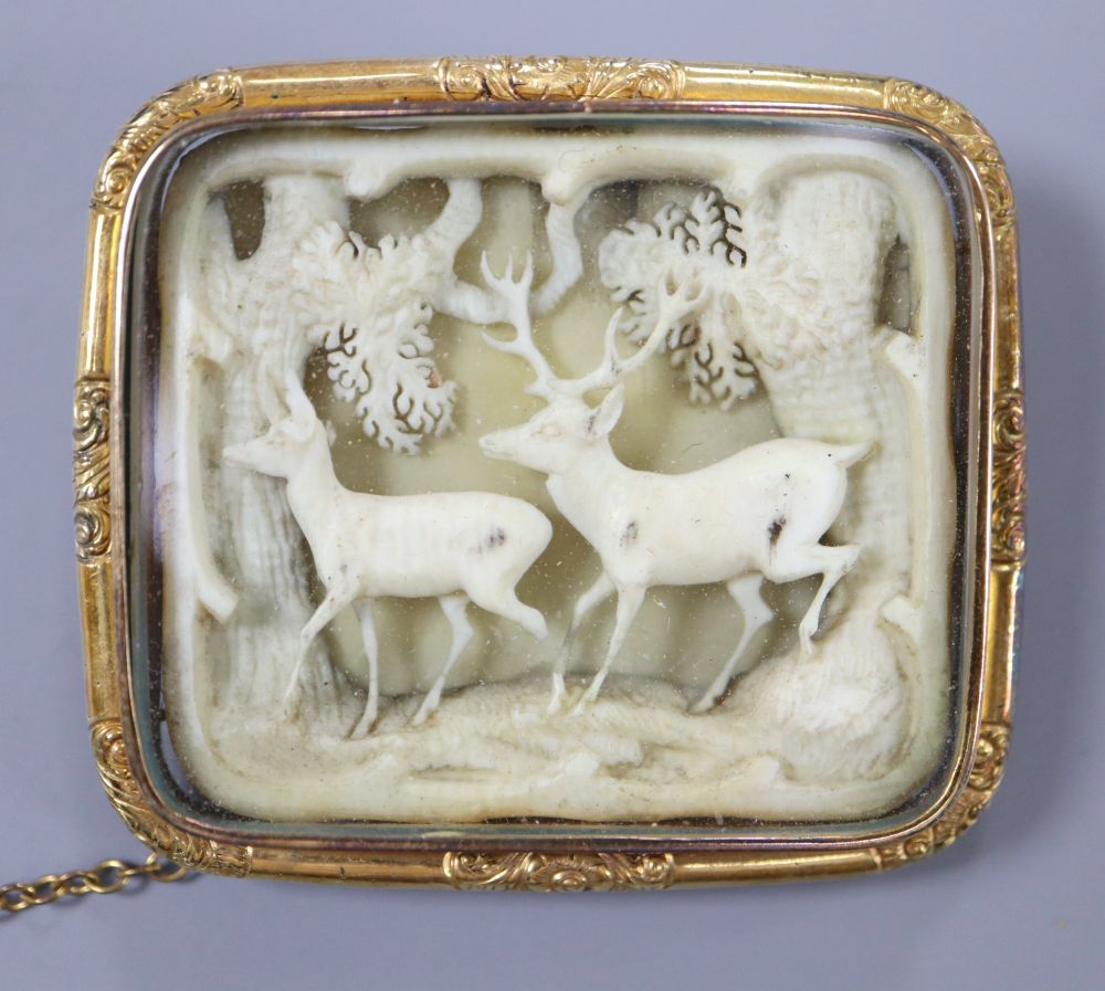 A 19th century Austro-German yellow metal framed brooch, inset with carved ivory forest scene depicting two deer,