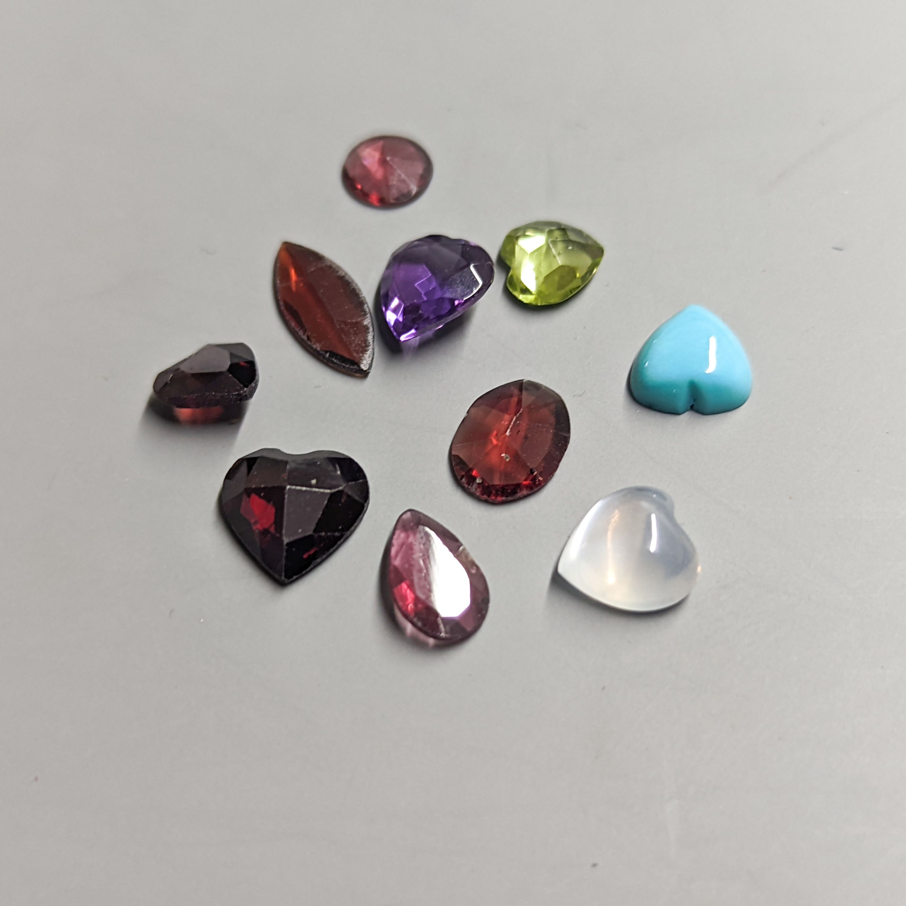 Nine assorted unmounted cut semi-precious gemstones including amethyst and garnet.