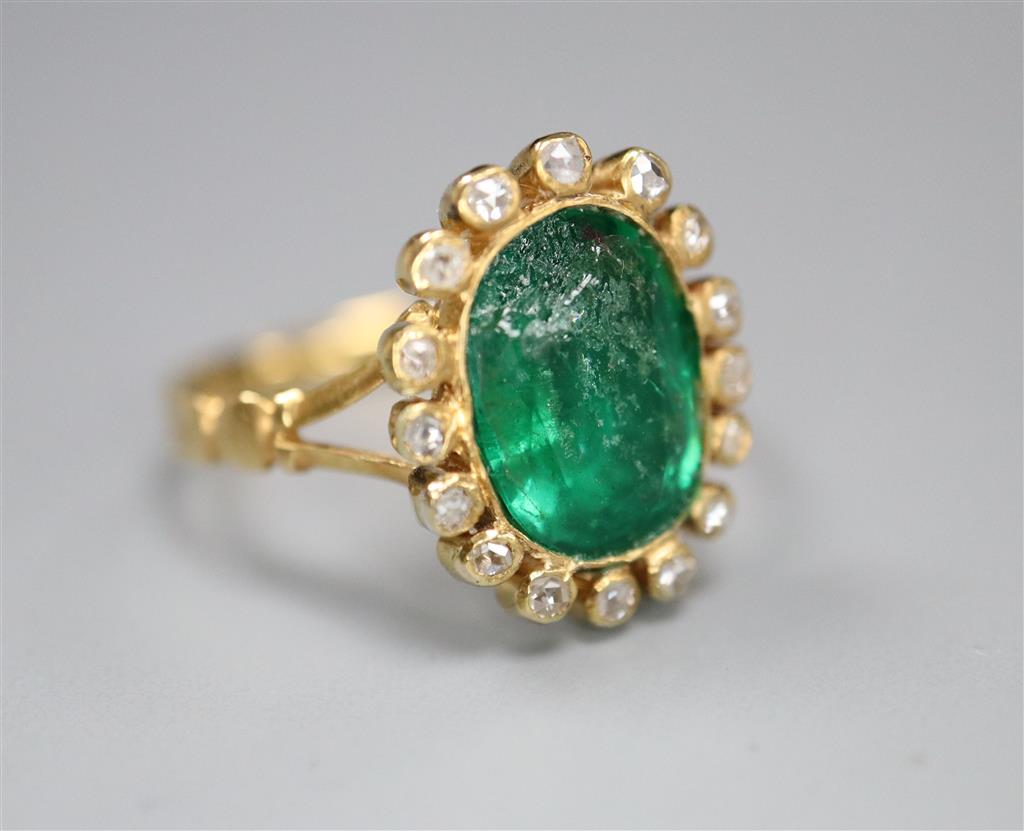 An early 20th century yellow metal, emerald and diamond set oval cluster ring, size M, gross 4 grams (emerald badly chipped).