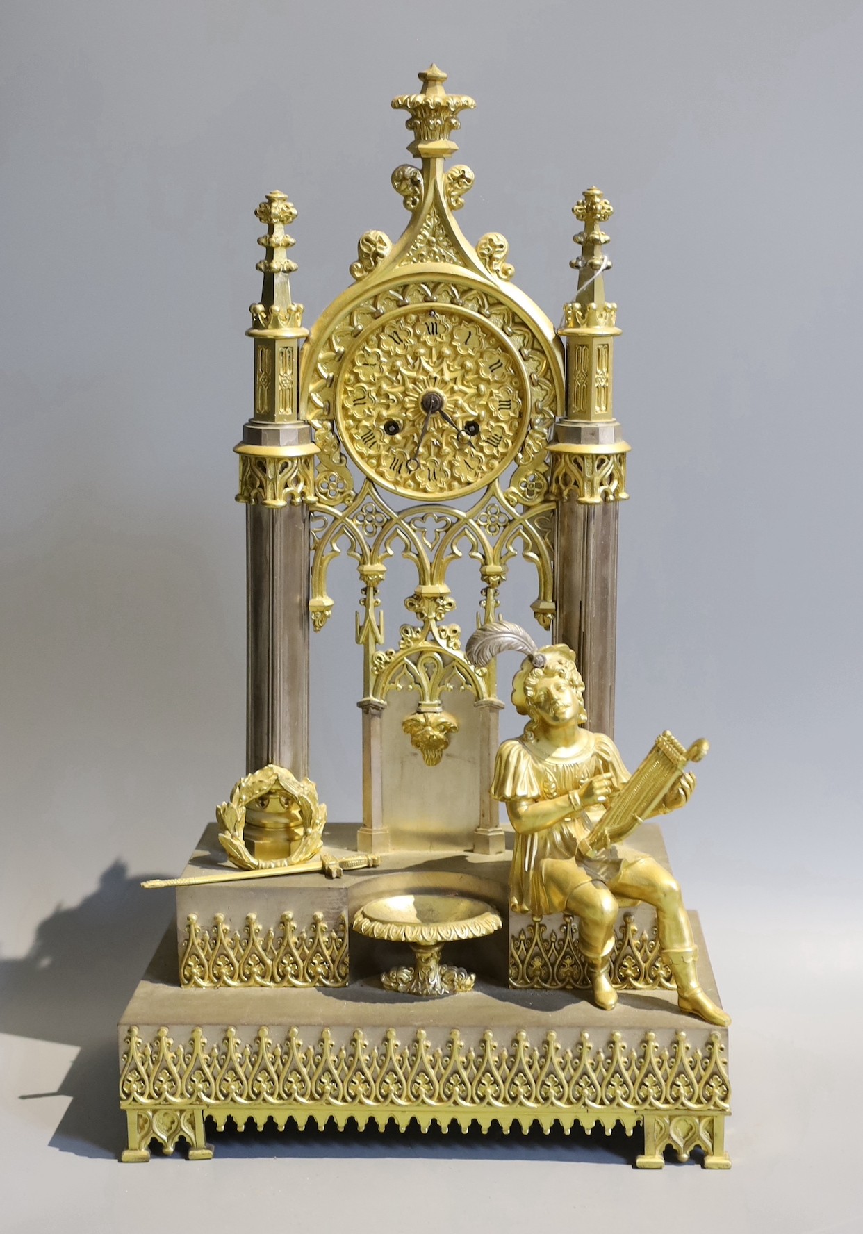 An early 19th century French silvered and gilt metal architectural 8 day mantel clock cast with a seated cavalier with lyre. Height 45 cms.