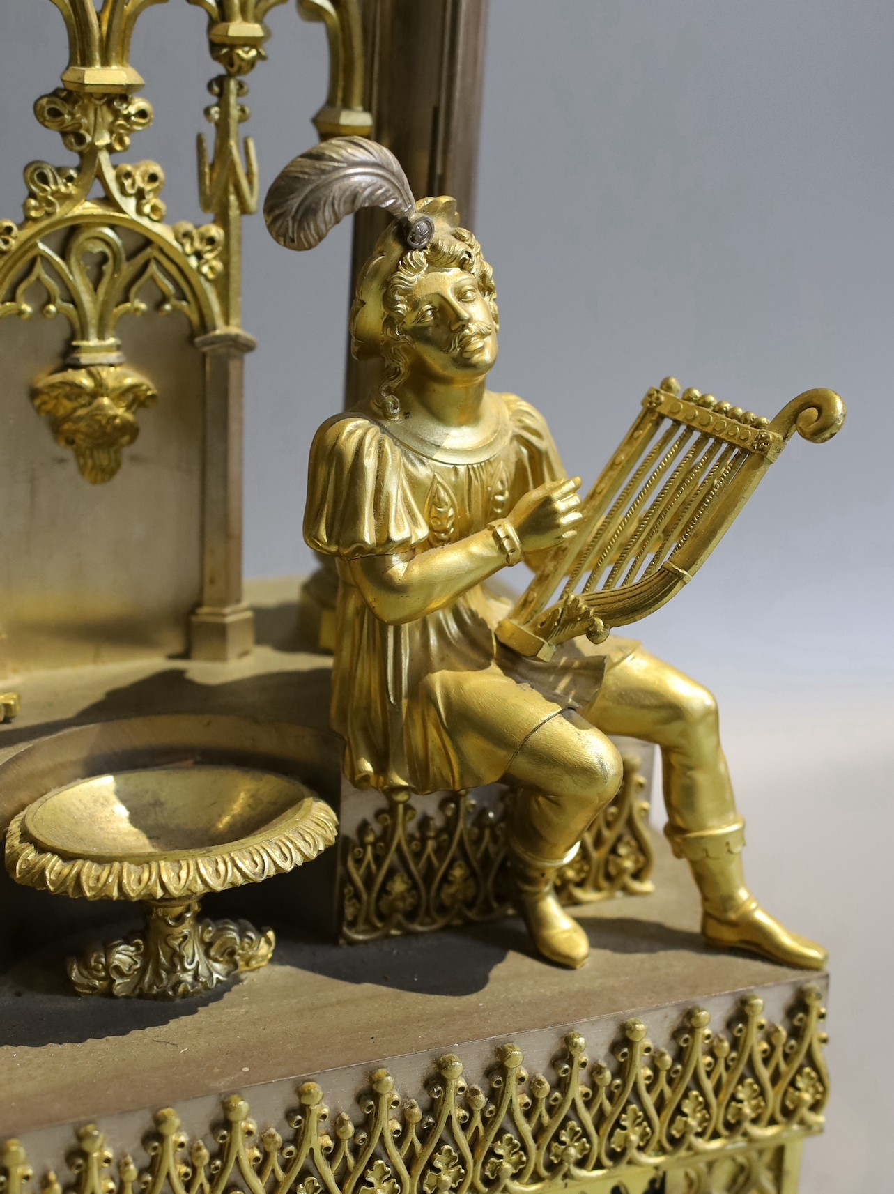 An early 19th century French silvered and gilt metal architectural 8 day mantel clock cast with a seated cavalier with lyre. Height 45 cms.