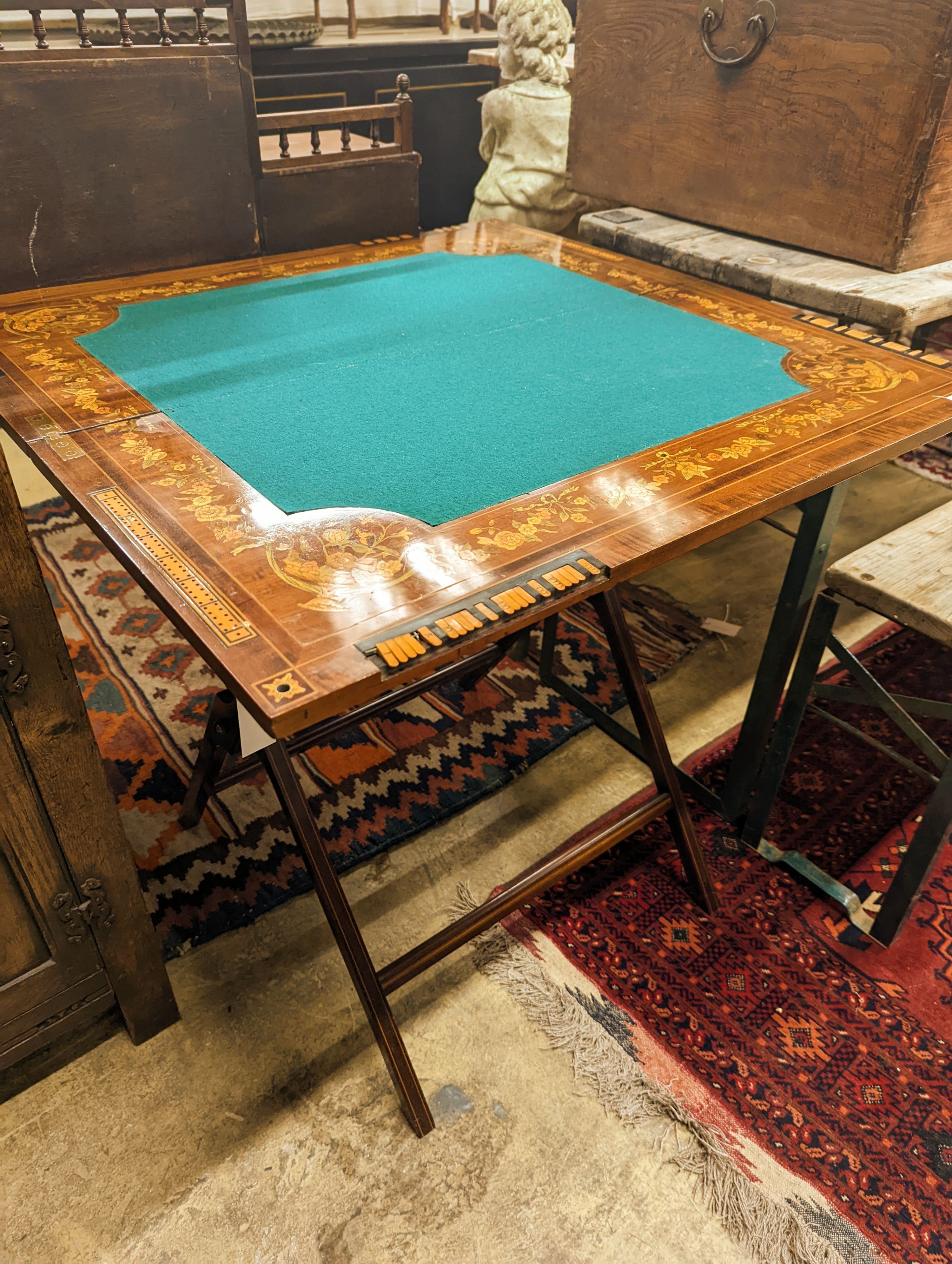 An Edwardian marquetry inlaid mahogany folding games table by W. Thornhill & Co., London, the interior baize lined surface with cribbage board and hinged markers, width 76cm, height 76cm