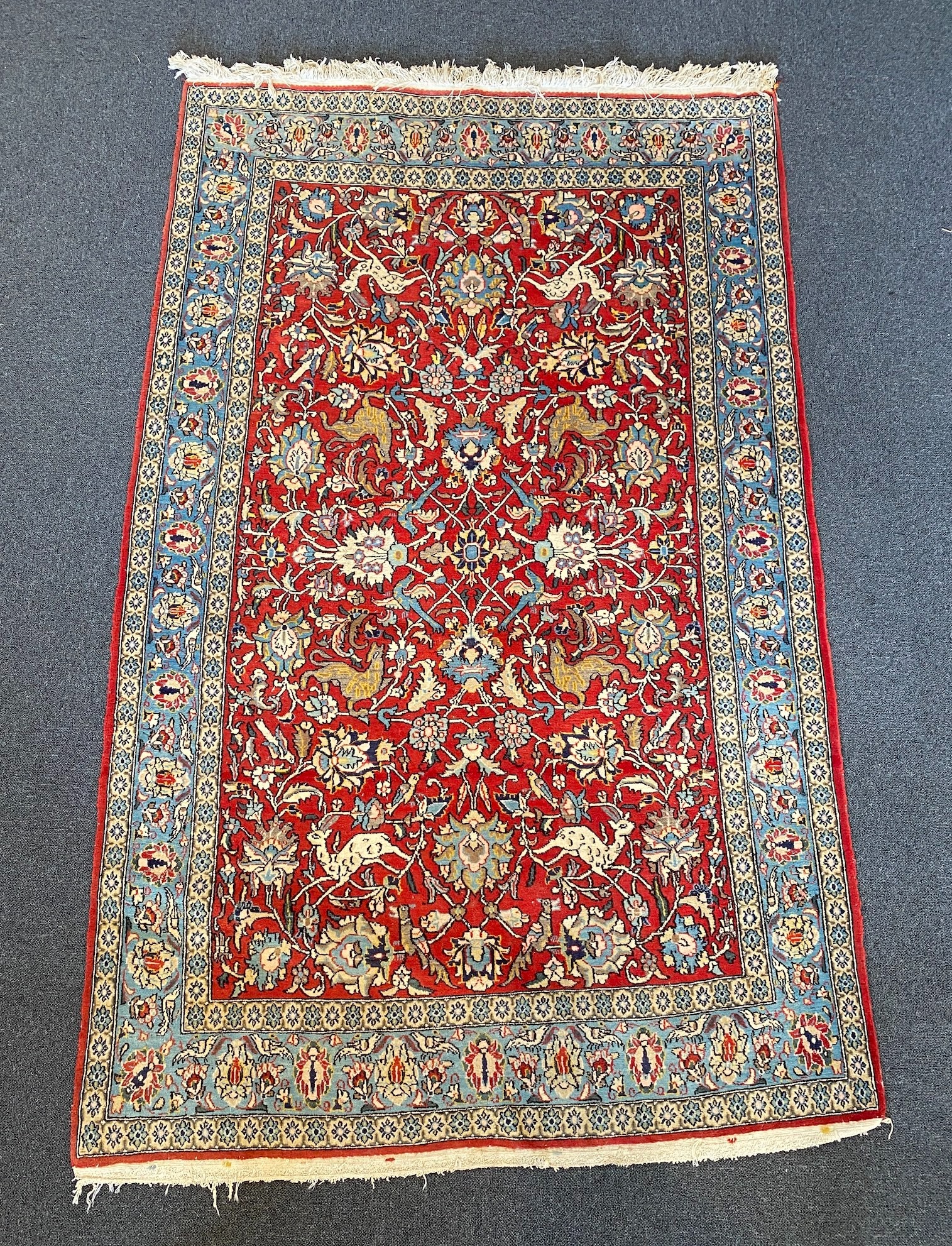 A Persian Qum red ground rug woven with animals and exotic birds among stylised flower heads 220 x 125 cms