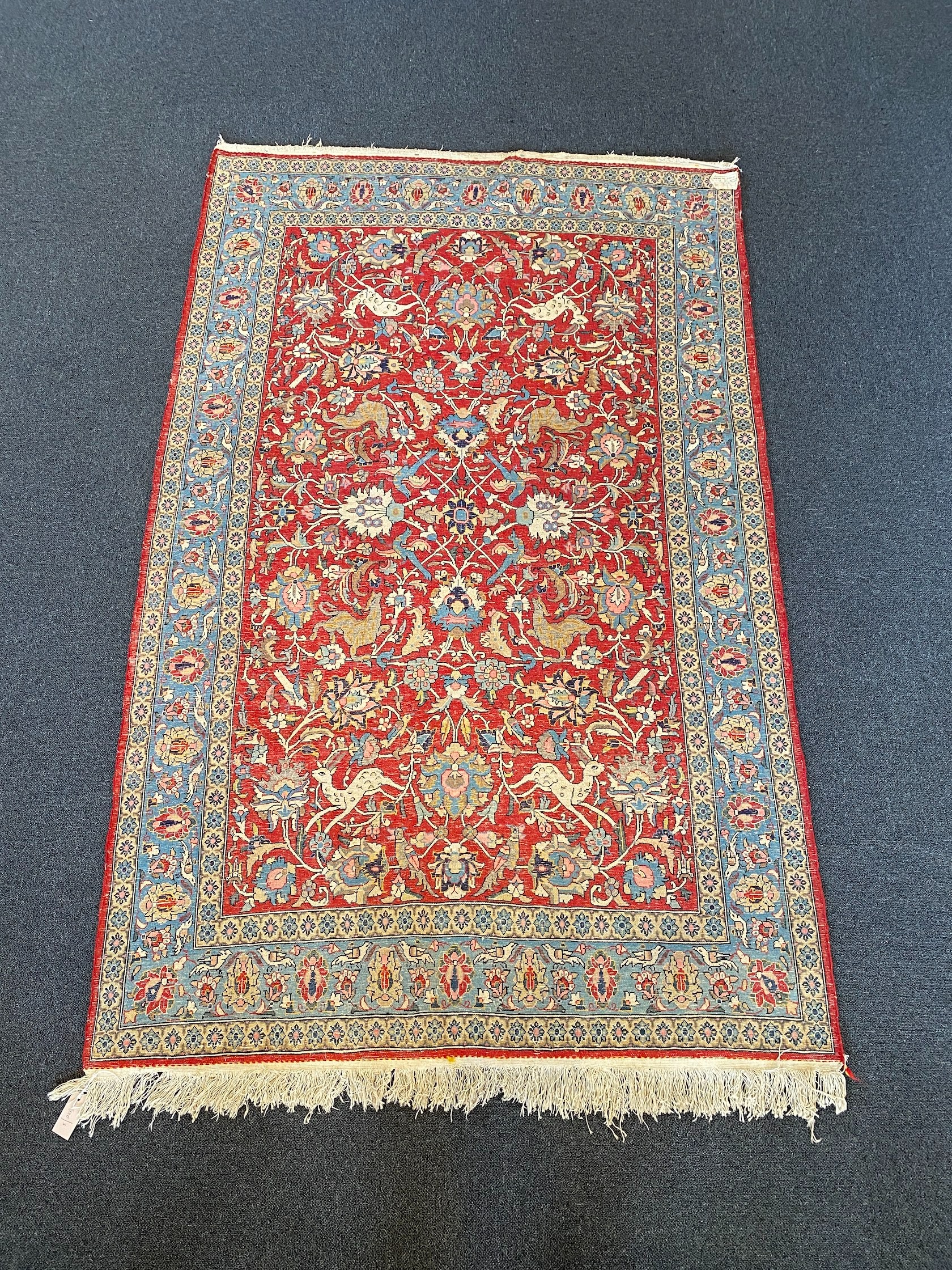 A Persian Qum red ground rug woven with animals and exotic birds among stylised flower heads 220 x 125 cms