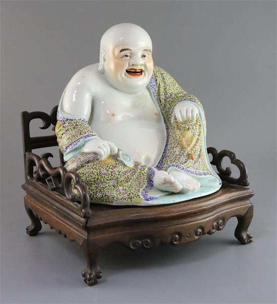 A Chinese famille rose seated figure of Budai, Republic period, H. 27cm, excluding hongmu throne stand A Chinese famille rose seated figure of Budai, Republic period, H. 27cm, excluding hongmu throne stand