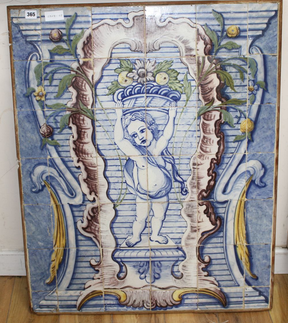 A Continental maiolica tile panel, depicting a putto holding aloft a basket of fruit, overall 90 x 72cm