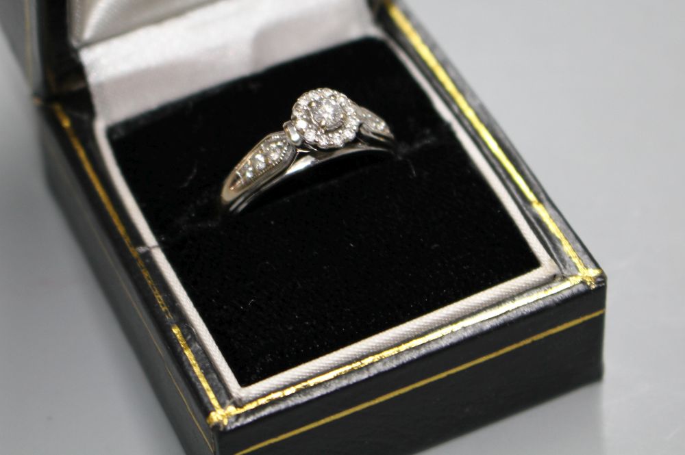A modern 18k white metal and diamond cluster flower head ring, with diamond set shoulders,