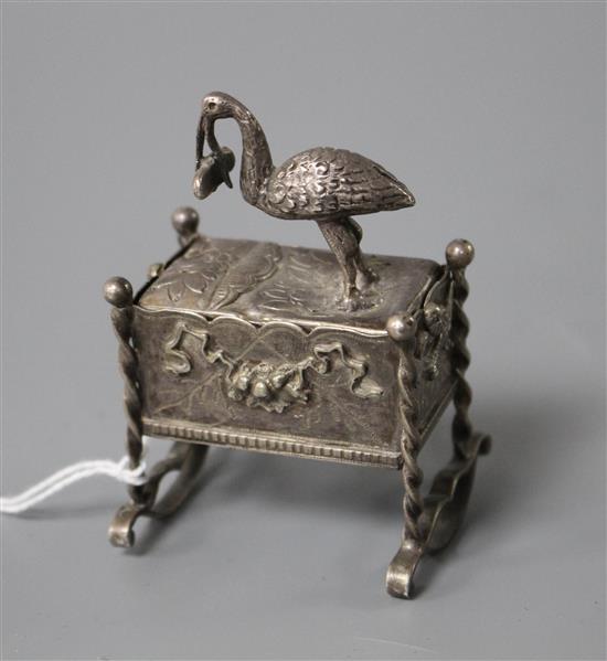An early 20th century continental white metal novelty box and cover, modelled as a stork with baby upon a cradle,