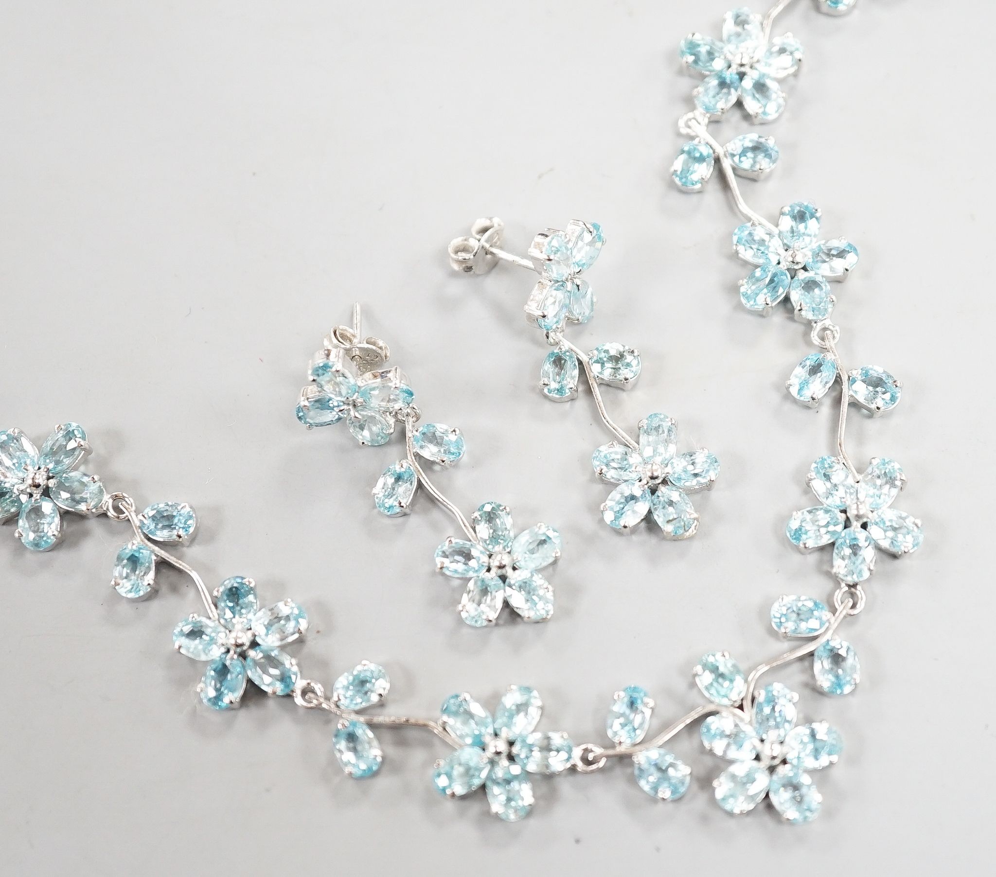 A modern 925 and blue zircon suite of jewellery, comprising a flower head cluster necklace and a pair of matching earrings.