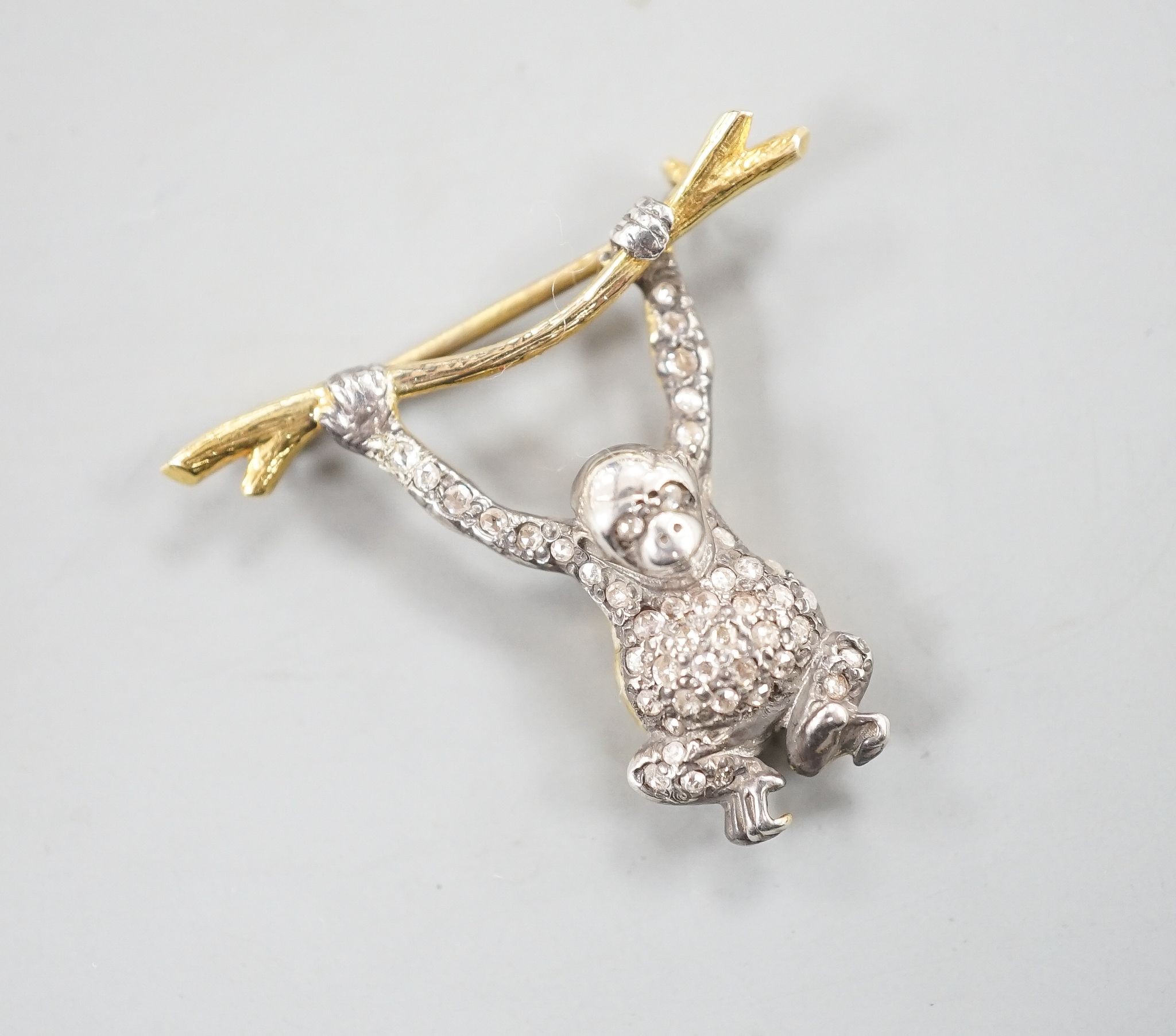 A Victorian style novelty white and yellow metal, diamond chip set brooch, modelled as a monkey hanging from a branch