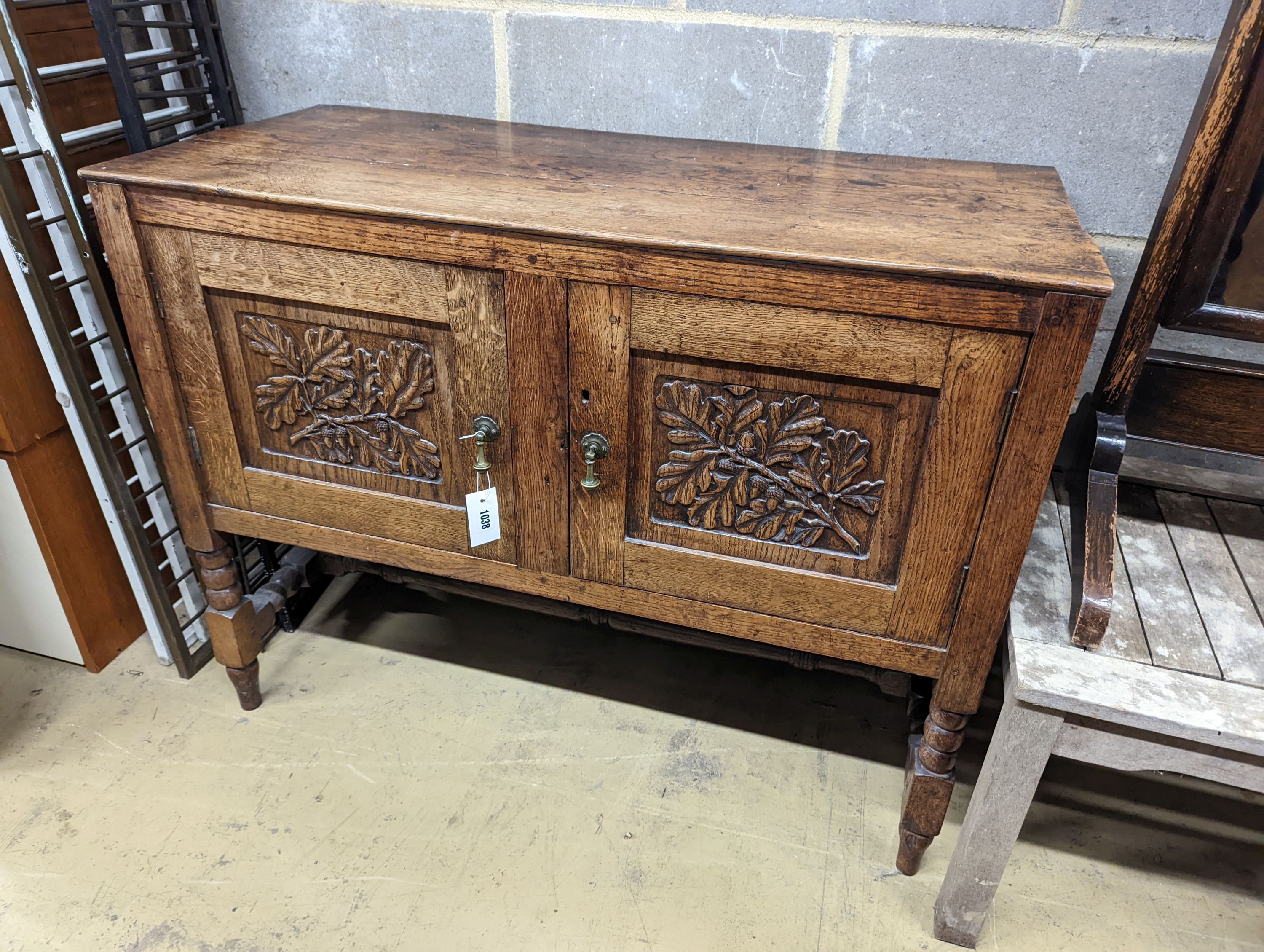 An early 20th century Arts & Crafts oak two door cabinet, carved with oak branches, width 100cm, depth 45cm, height 77cm