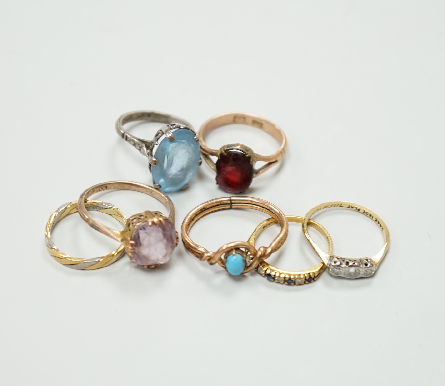 Seven assorted dress rings, comprising an 18ct gold three stone diamond ring, size M, a 9ct gold dress ring with associated worn red stone, size P, a silver ring with blue stone, size I, a 9ct gold and amethyst ring, siz