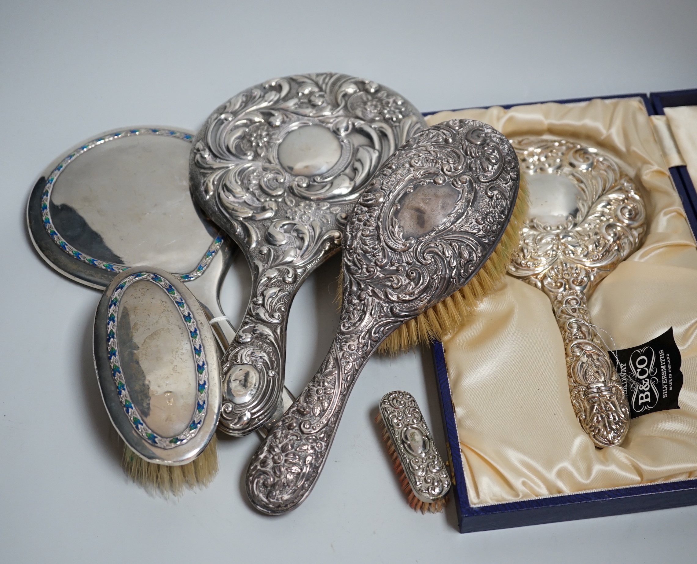 A George V silver and enamel mounted hand mirror and brush, B & Co, Birmingham, 1927?, two other silver mounted hand mirrors and two similar brushes.                                                                       
