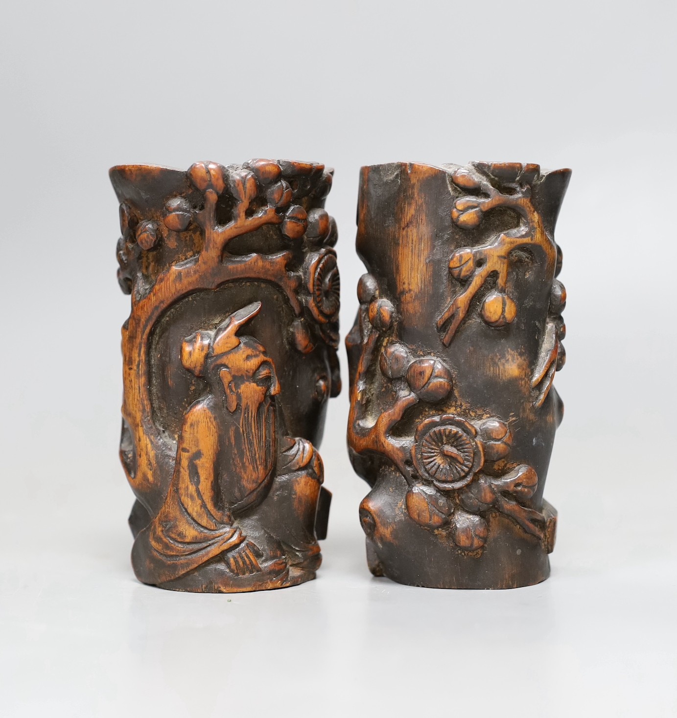 A pair of Chinese carved bamboo brush pots, late Qing dynasty, carved in high relief with a sage beneath a prunus tree, 11cms high                                                                                          