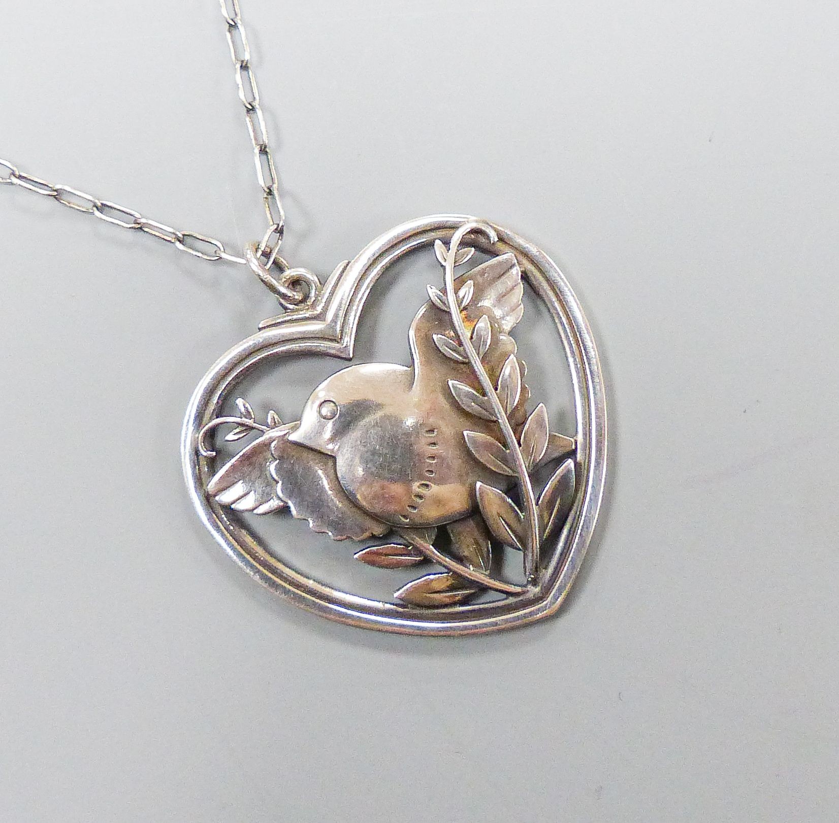 A Georg Jensen sterling 'Robin and frond' heart shaped pendant, no. 97, 38mm, on a white metal chain, 57cm.                                                                                                                 