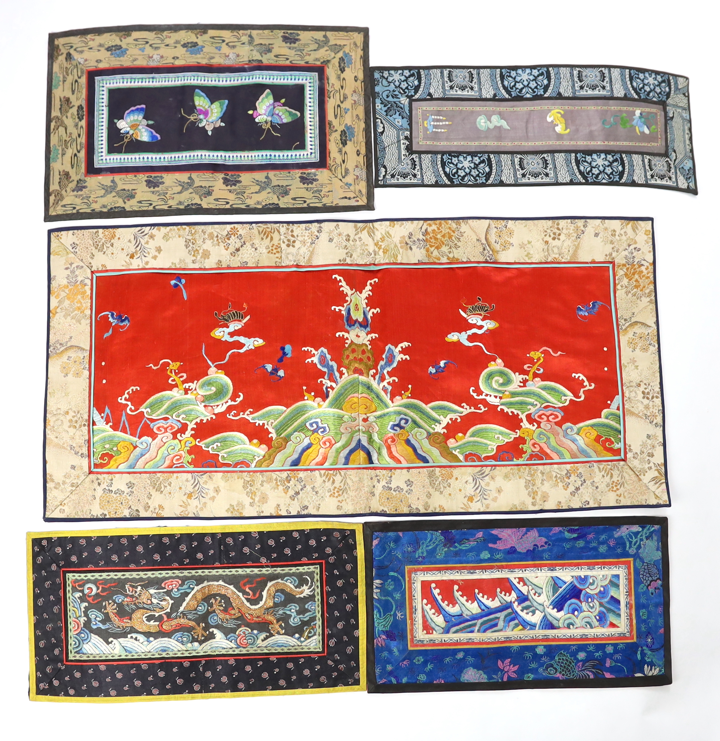 A Chinese late Qing dynasty red silk and polychrome embroidered lishui wave and flaming pearl panel, another smaller metallic dragon panel, an ornate butterfly panel and two other smaller embroidered panels with auspicio