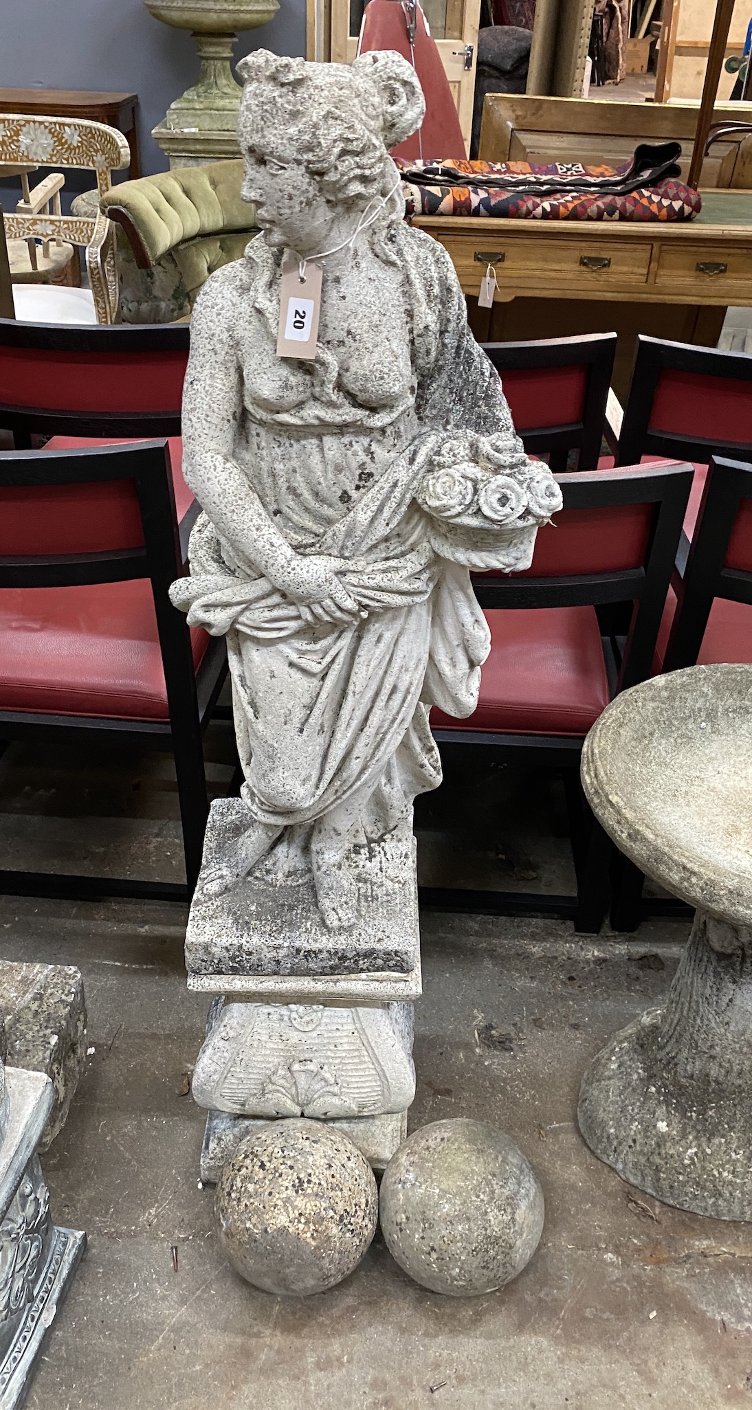 A reconstituted stone garden statue of lady holding a basket on flowers, on square plinth, height 130cm                                                                                                                     