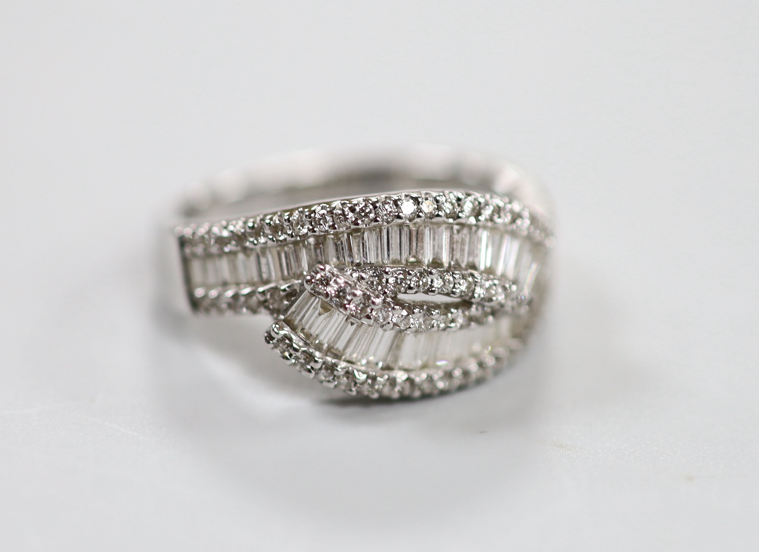 A modern 18ct white gold, baguette cut and diamond chip cluster set crossover ring, size O, gross weight 4.7 grams.                                                                                                         