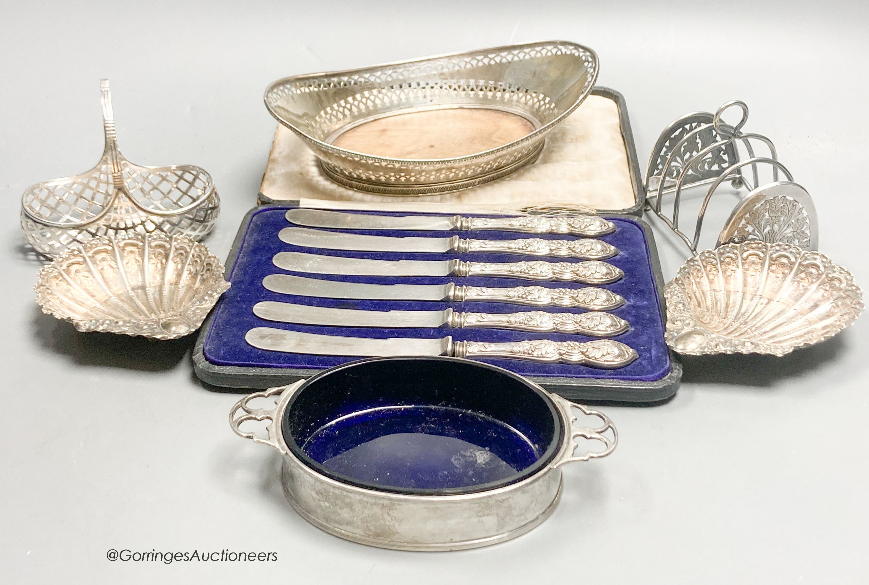 A George V silver two handled butter dish, with blue glass liner, a white metal basket, a pair of Victorian shell dishes, a French white metal dish, white metal toast rack and cased tea knives.                           