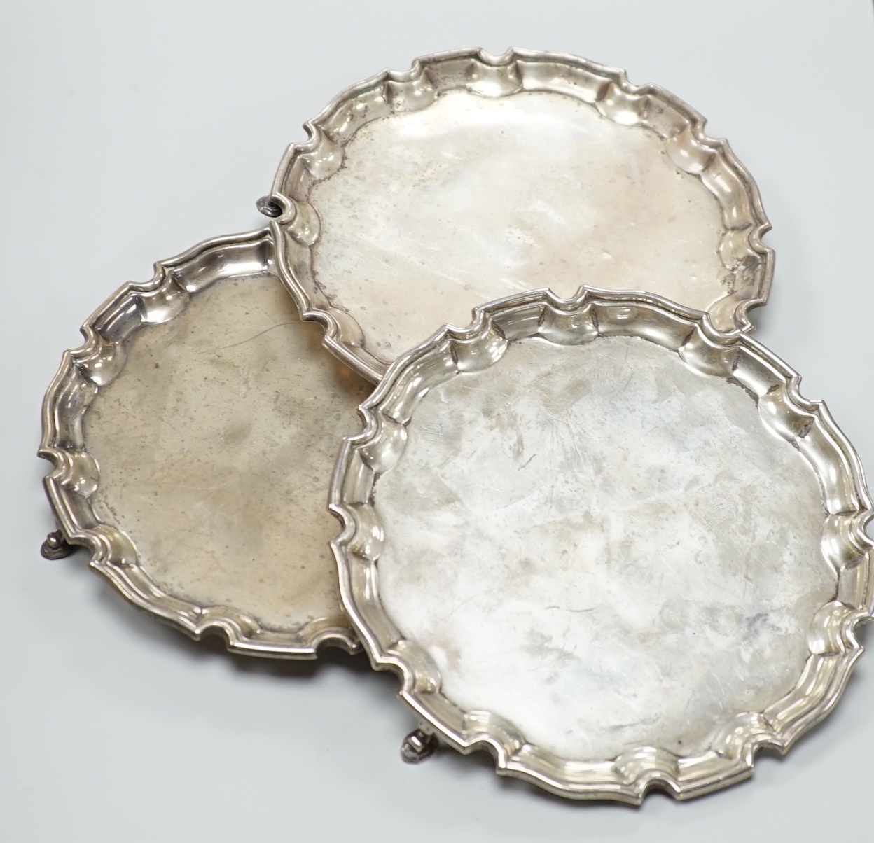 A matched set of three George V silver waiters, Mappin & Webb, Birmingham, 1913,1914 and 1921, with pie crust borders, on three hoof feet, 15.2cm, 12oz.                                                                    
