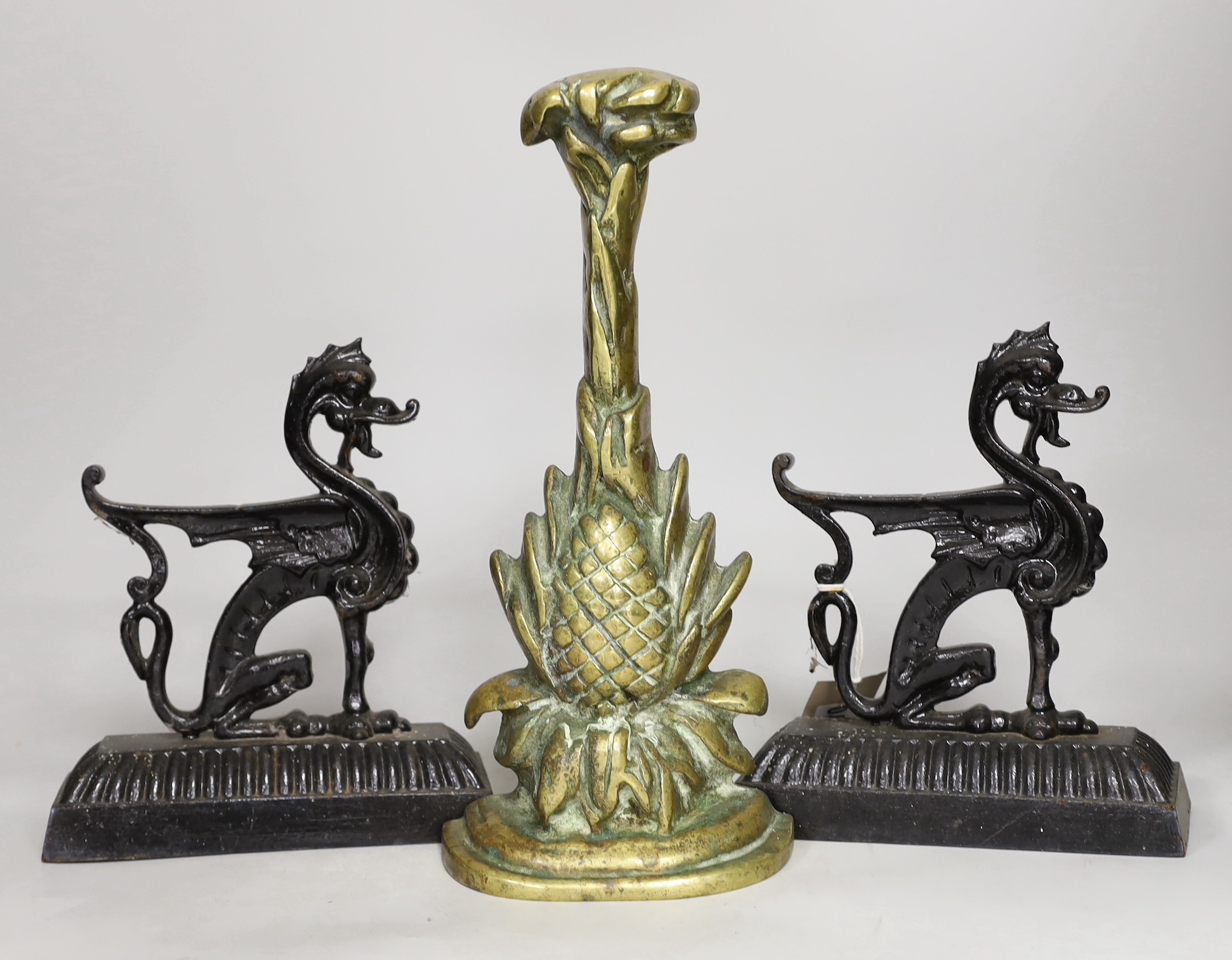 A pair of cast iron seated lion dog doorstops, together with A brass pineapple shaped door porter. Tallest 31cm                                                                                                             