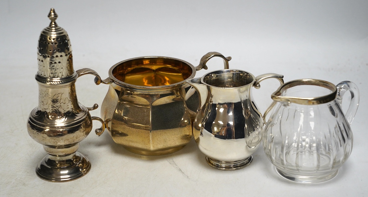 A George V silver two handled sugar bowl, Edward Barnard & Sons Ltd, London, 1926, two silver cream jugs including mounted glass and a white metal pepperette. Condition - poor to fair                                     