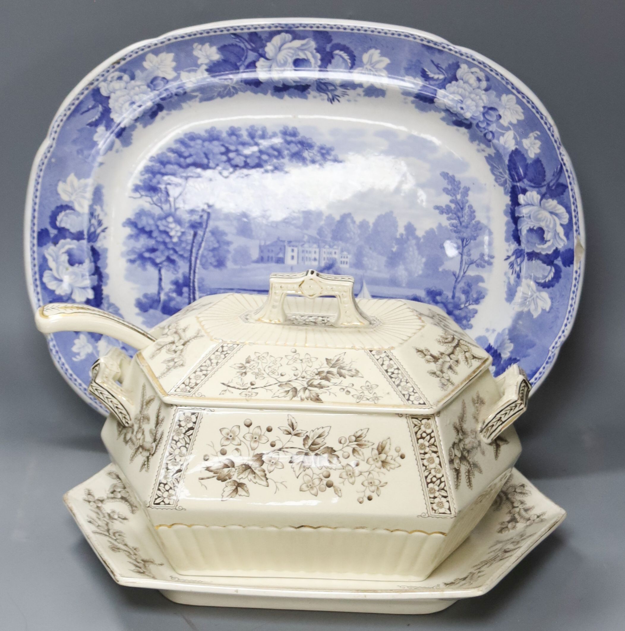 A late 19th century Staffordshire blue and white transfer-printed oval meat dish, ‘The Rokery’, depicting a country house with lake and figures, W 44cm and an octagonal 'Flora' creamware soup tureen with ladle and stand 