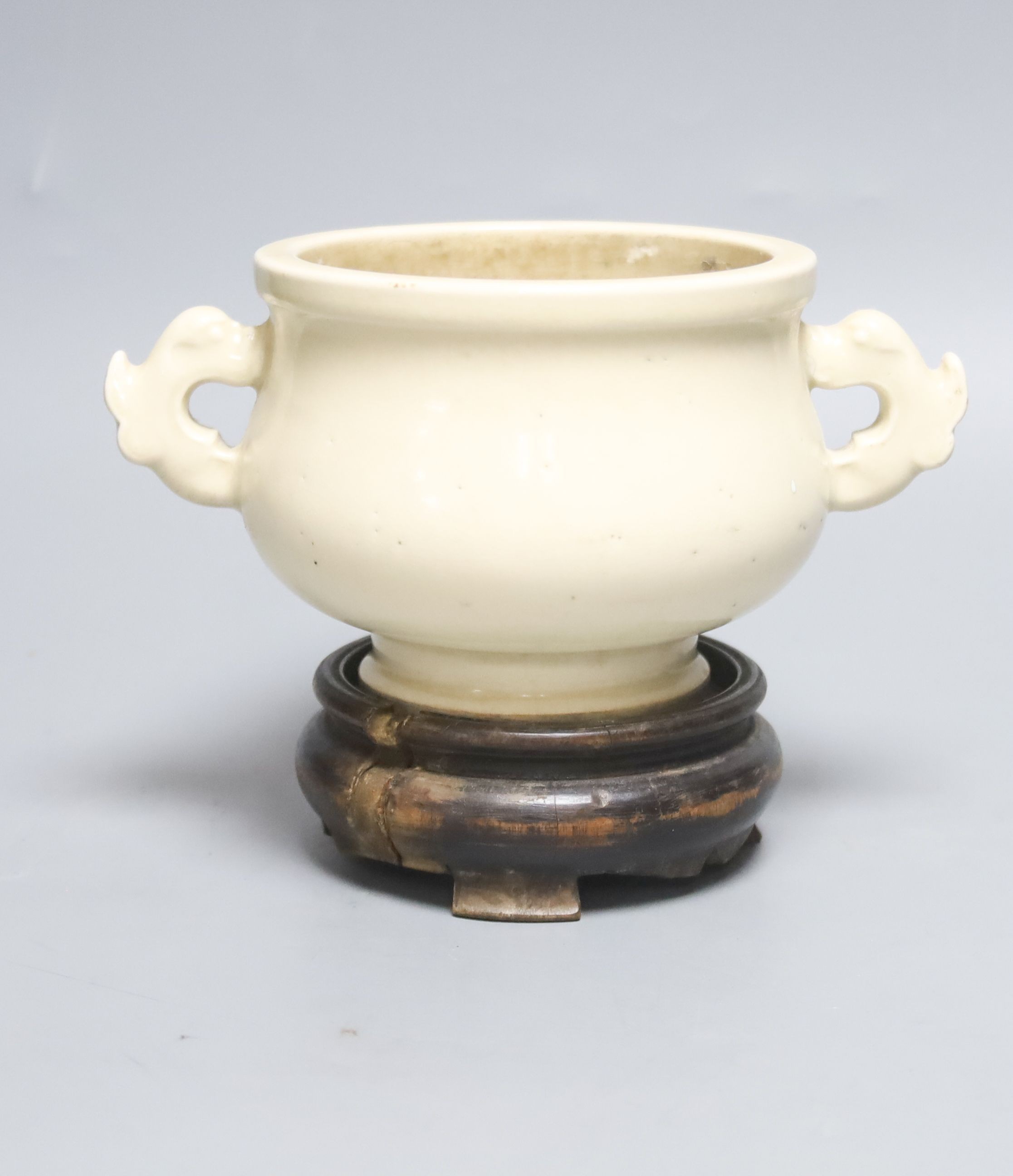 A Chinese cream crackle glazed censer, Qing dynasty, with dragon handles, 19 cm wide, on hardwood stand, W 18cm                                                                                                             