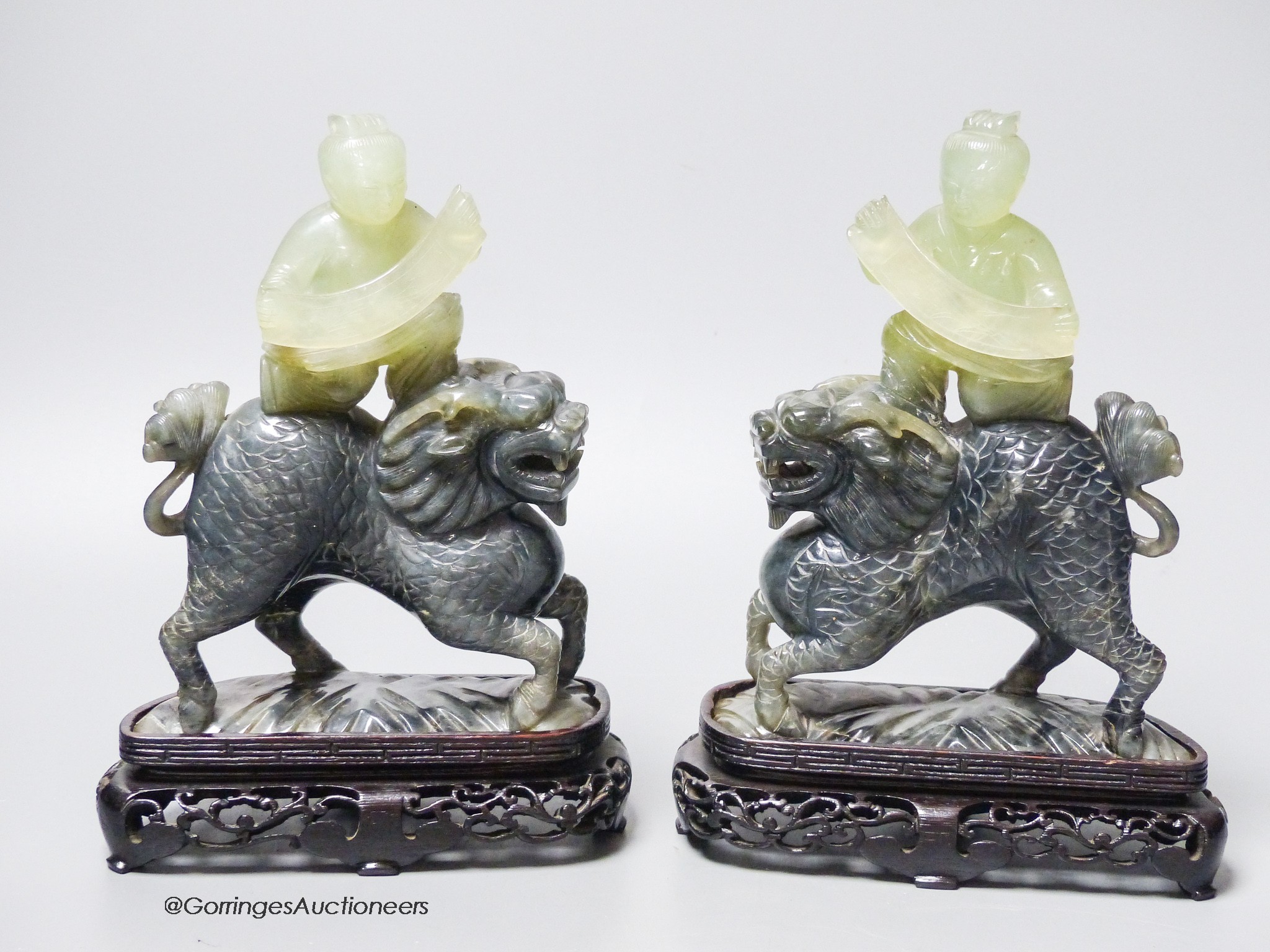 A pair of Chinese bowenite Jade figures of boys riding a qilin, mid 20th century, wood stands                                                                                                                               