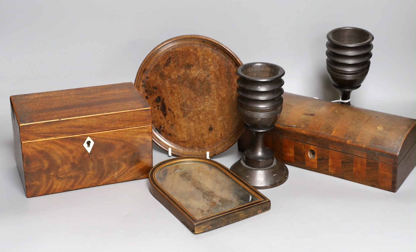A George III inlaid mahogany tea caddy, a Victorian satinwood and rosewood domed topped glove box, a burr wood circular tray, a George III inlaid mahogany domed topped easel mirror and a pair of turned hardwood cups     