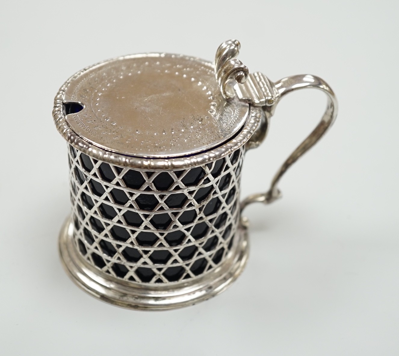 A Victorian pierced silver drum mustard pot by George Fox, London, 1872, with blue glass liner, (handle repair), height 76mm.                                                                                               