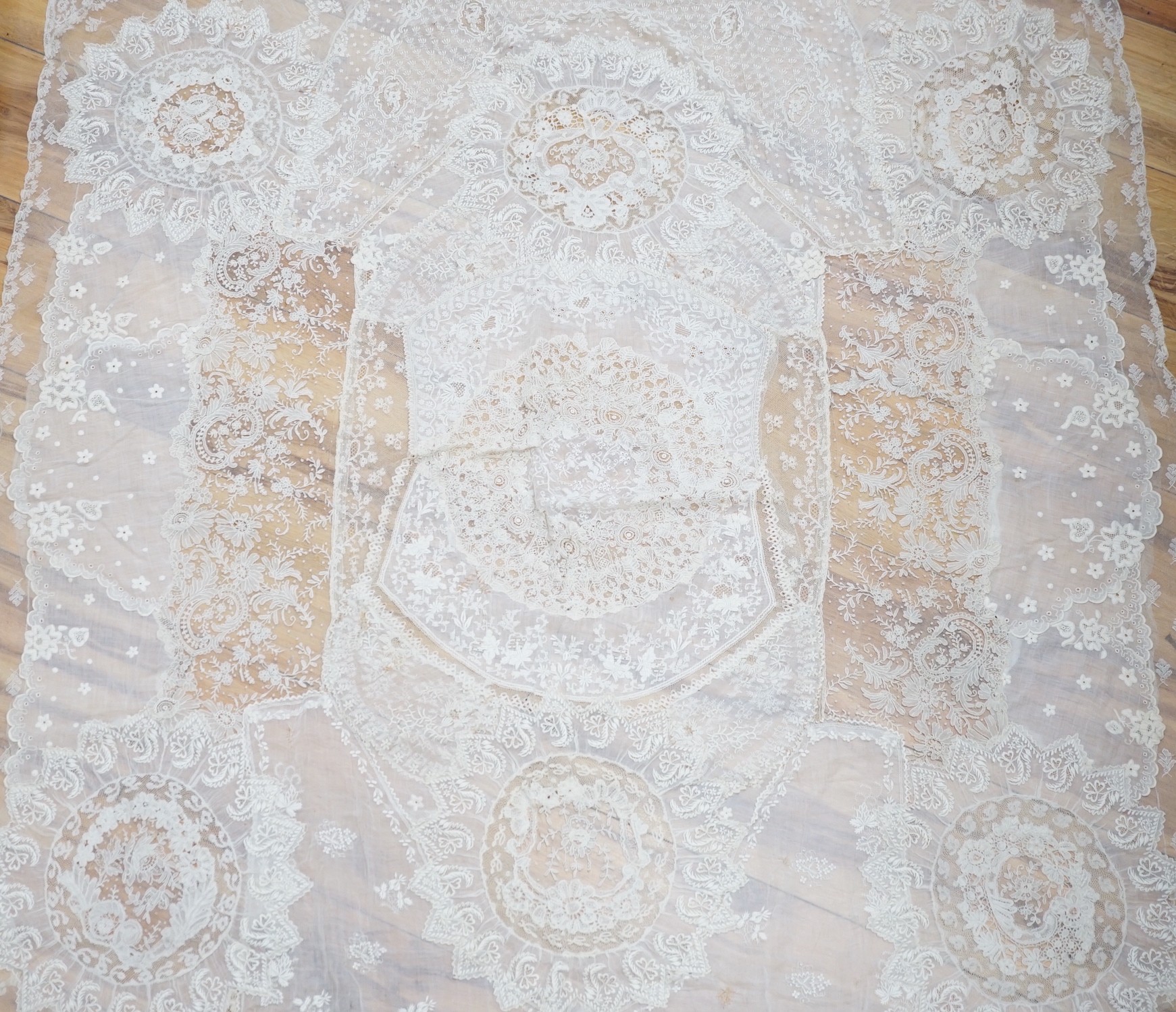 A late 19th century Normandy lace table cover of hand spun linen, hand white worked, with Brussels Point de Gaze insertions and bobbin lace edging, together with two feathers and a net veil                               