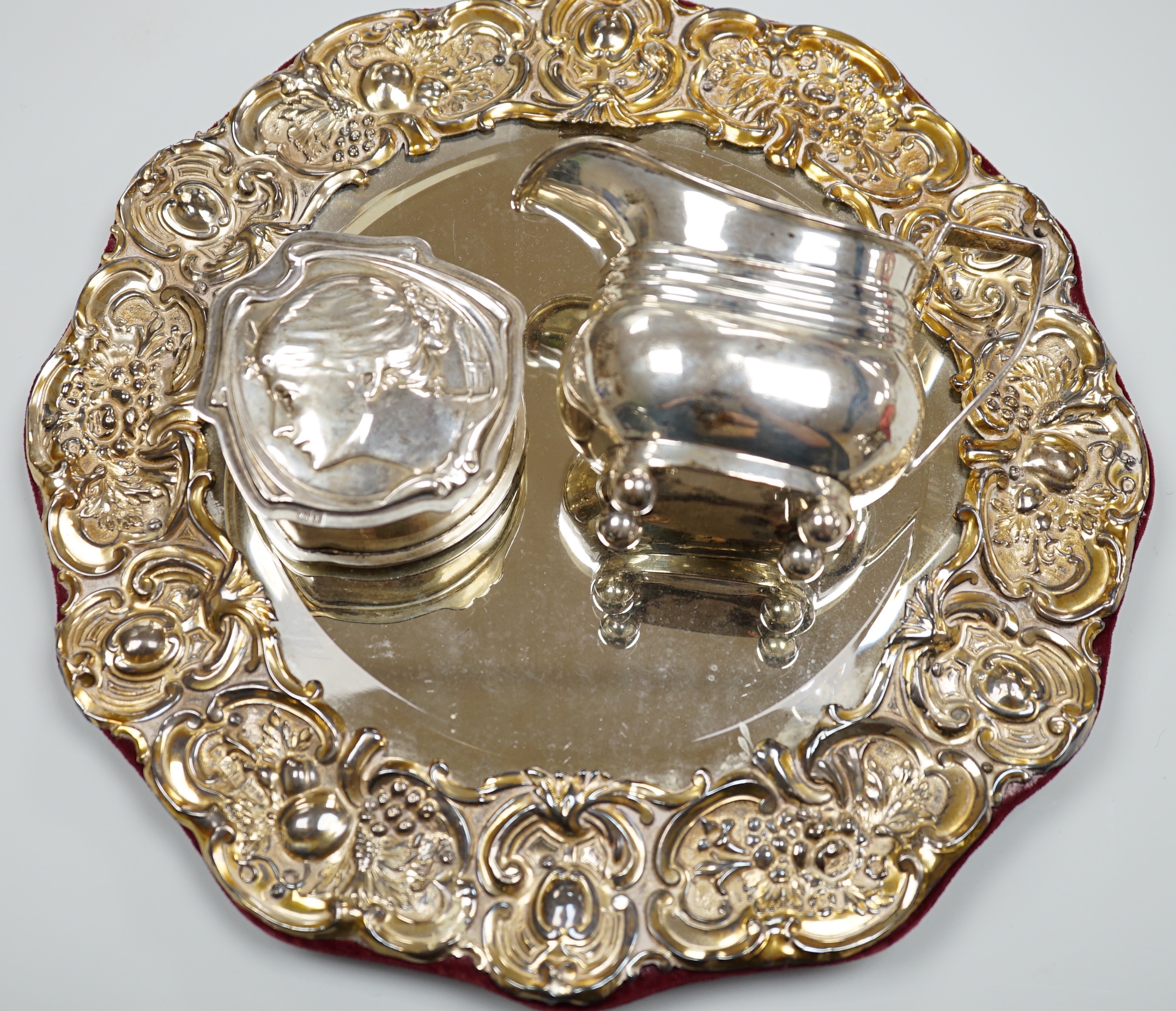 An Edwardian silver mounted circular easel mirror, Walker & Hall, 26.5cm, an Art Nouveau silver trinket box, William Hutton & Sons, London , 1904 and a silver milk jug.                                                    