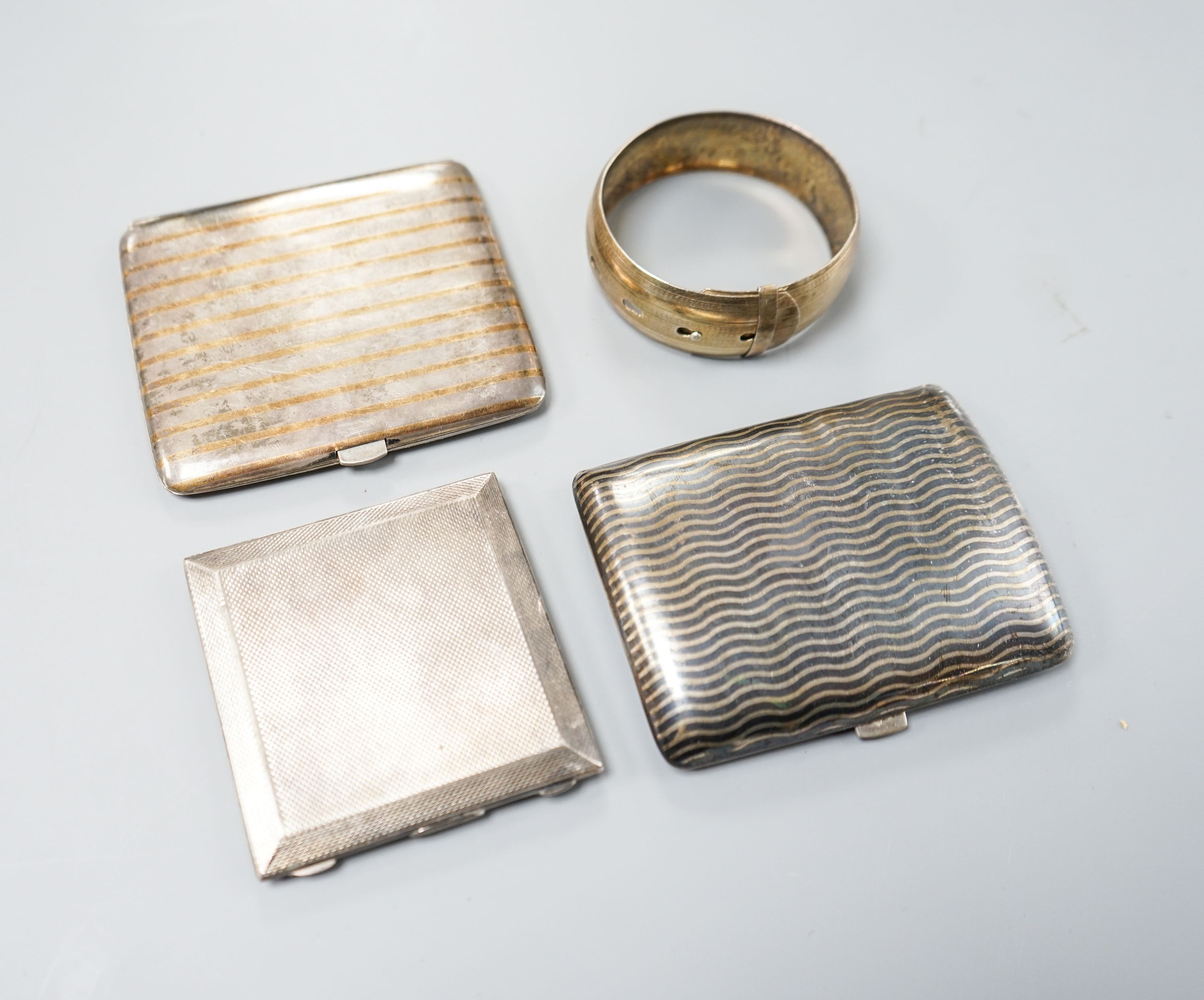 An 800 white metal and niello cigarette case,9cm, a Dutch gilt and white metal cigarette case, an engine-turned silver powder compact (a.f.) and a white metal bangle.                                                      