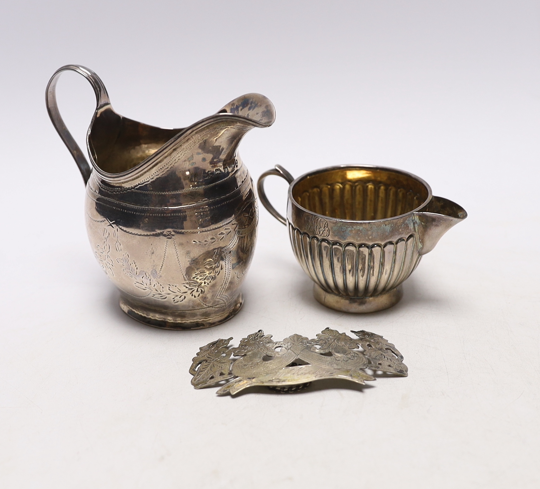 A George III silver helmet shaped cream jug, London, 1799 (a.f.), a Victorian silver cream jug by George Unite and a white metal whisky wine label.                                                                         