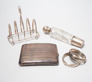 A French white metal cigarette case, a silver toast rack, a French white metal mounted glass scent bottle and a pair of French white metal napkin rings.                                                                    