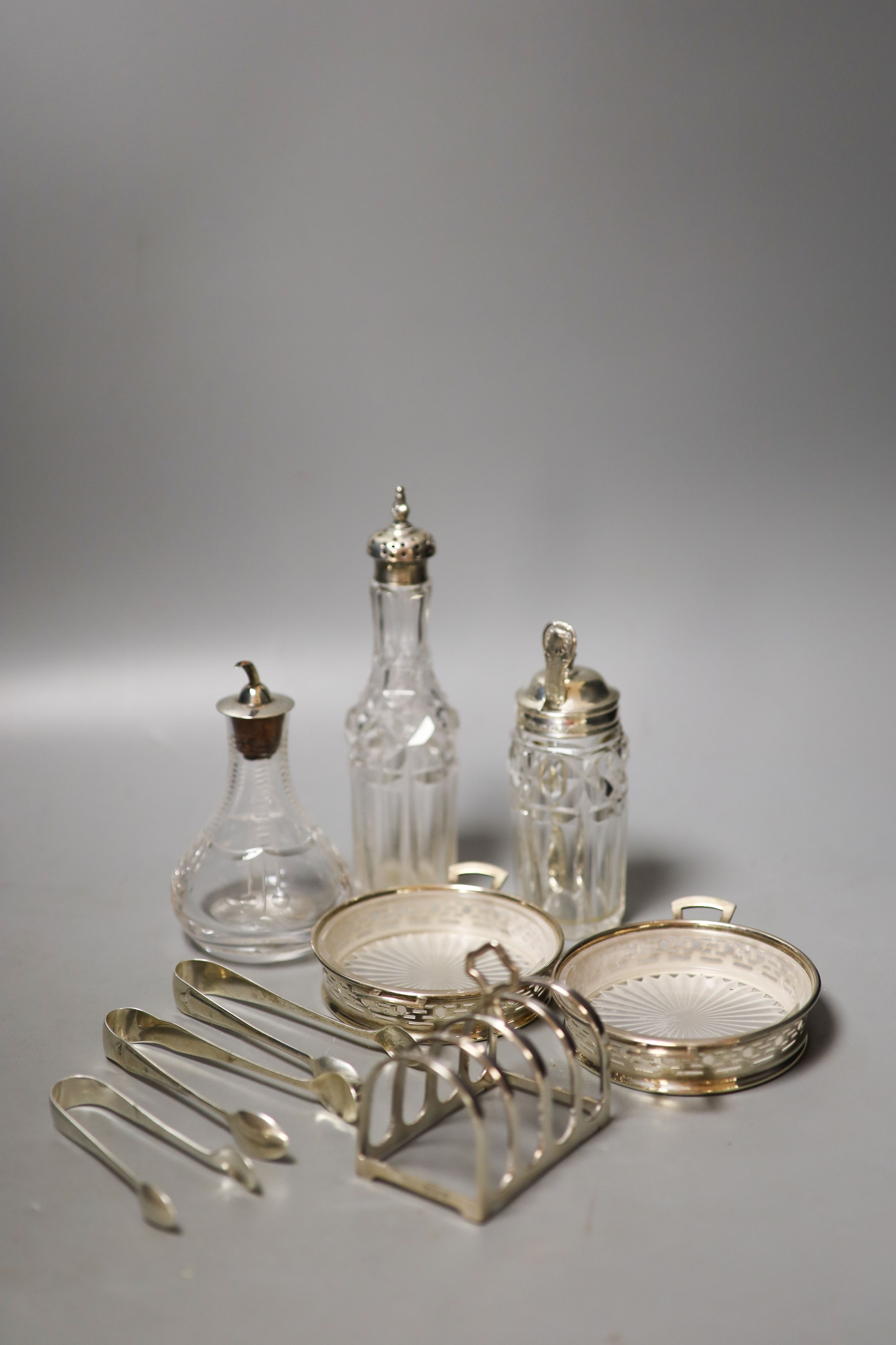 A pair of modern silver mounted glass butter dishes, a silver toastrack, three silver mounted glass bottles and three pairs of silver sugar tongs.                                                                          