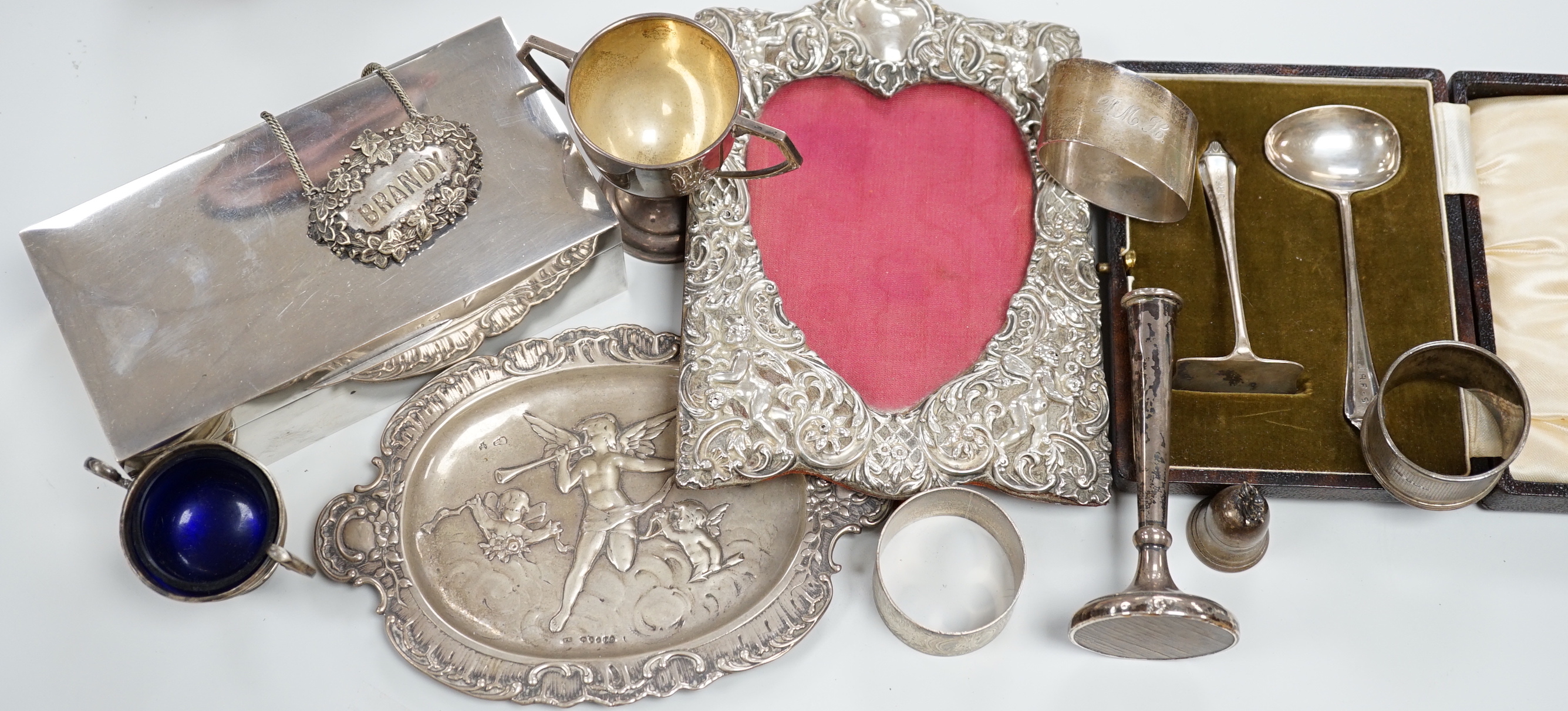 A modern silver mounted rectangular cigarette box, an Edwardian repousse silver mounted photograph frame, a small silver dish, small silver trophy cup, silver napkin rings etc.                                            