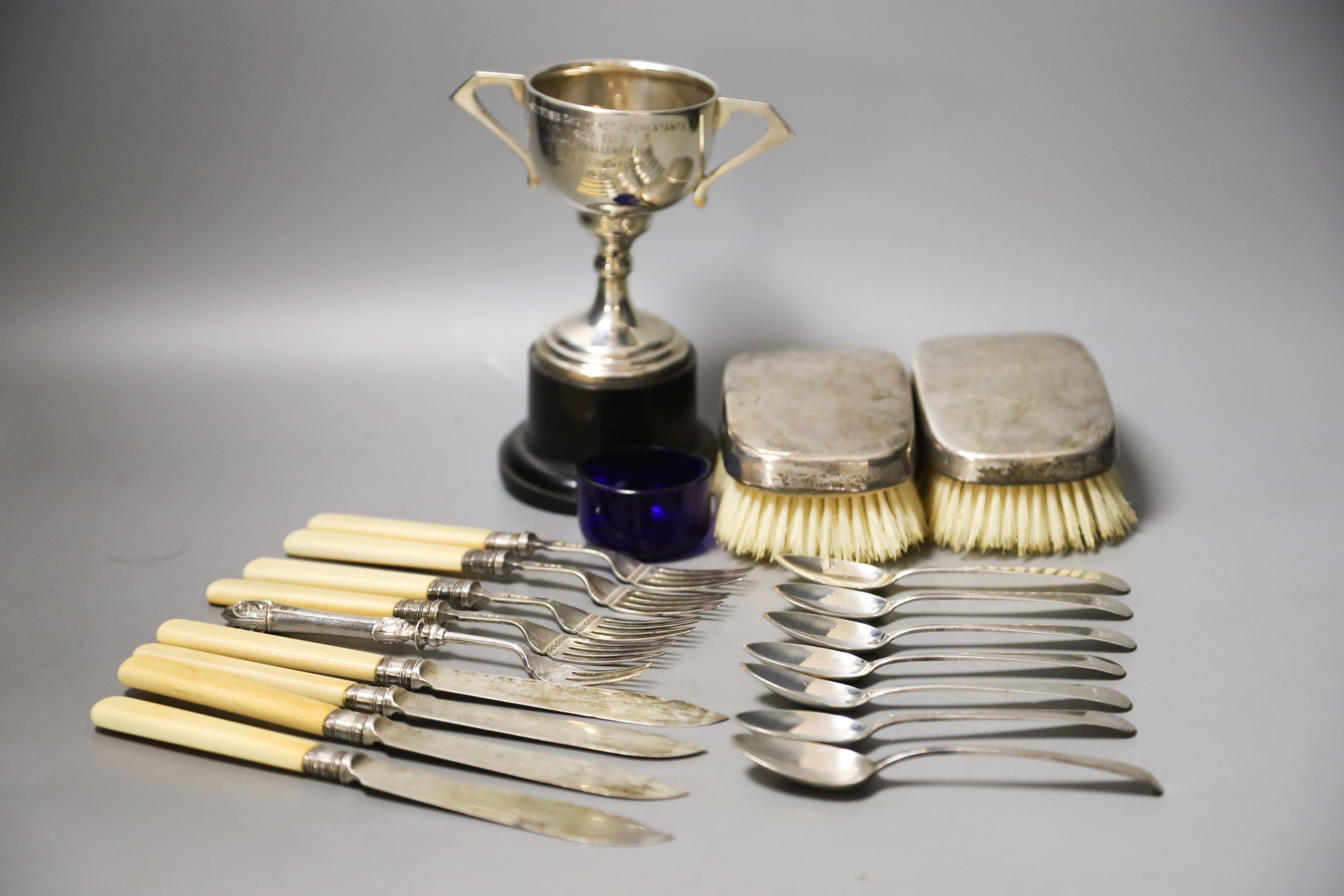 A pair of silver mounted clothes brushes, a silver two handled trophy cup and sundry flatware.                                                                                                                              