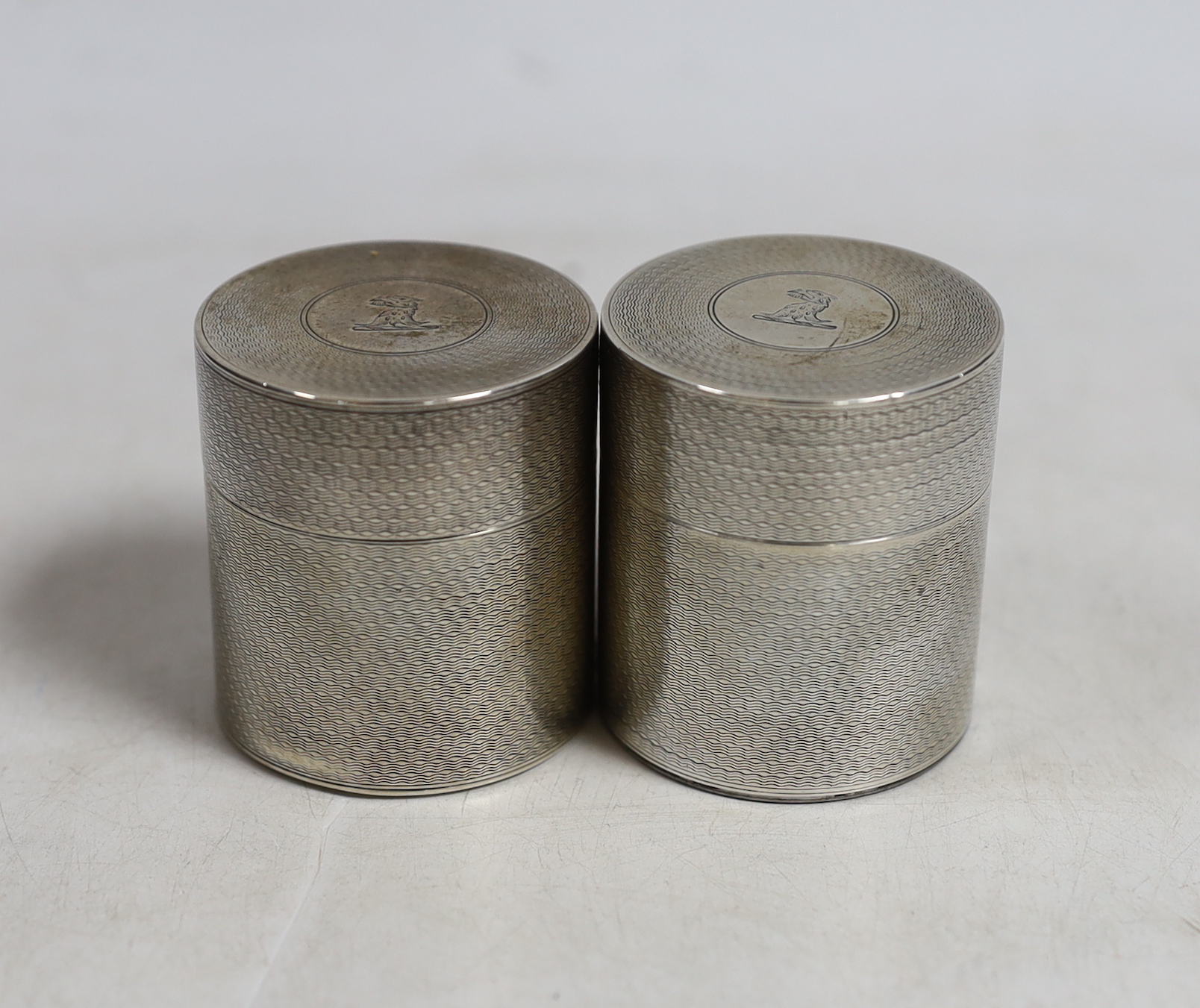 A George V engine turned silver cylindrical travelling inkwell?, by Samson Mordan & Co, London, 1910 with ribbed base and one other similar cylindrical box and cover, same date and maker, both with engraved crest, 48mm a